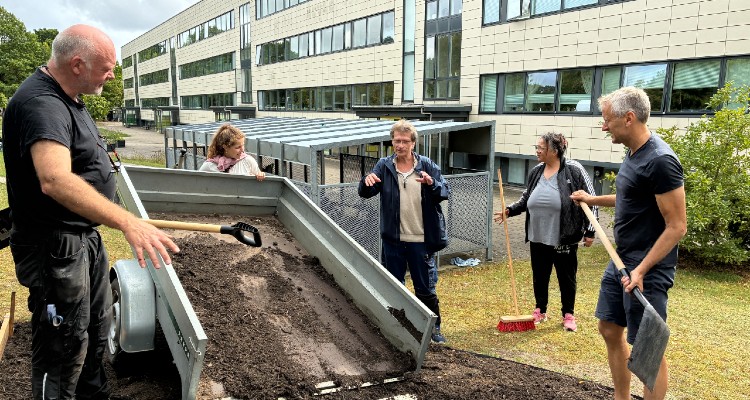 Medarbejdere og beboere arbejder sammen om at tømme en trailer med jord. I baggrunden ses Gyvelparken Ry. Foto: Skanderborg Kommune